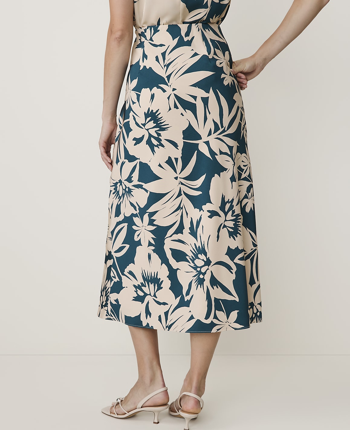 A woman in a floral skirt stands against a plain, light-colored background.