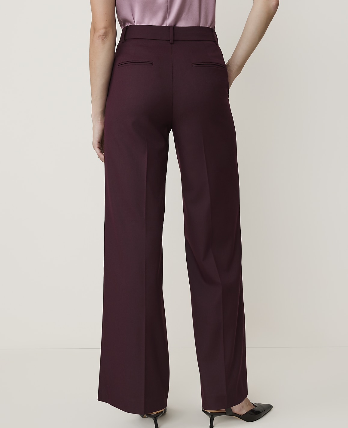 A person wearing burgundy wide-leg trousers and a satin top stands against a plain, light-colored background.