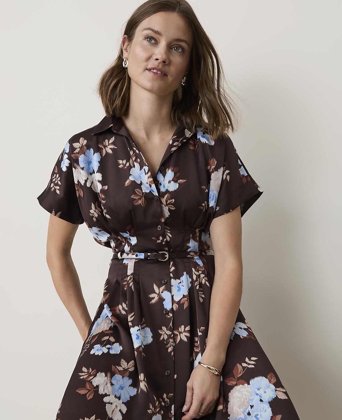 A woman in a brown floral dress with a cinched waist stands against a plain white background.