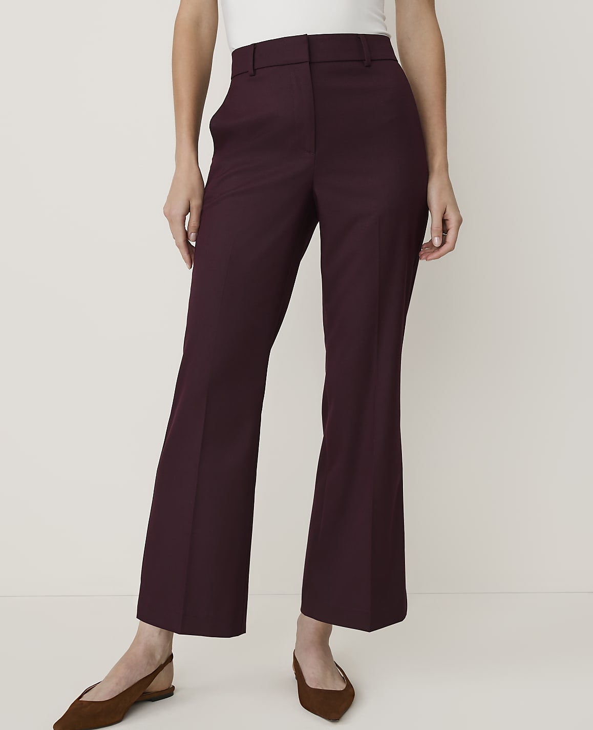 A person in maroon flared trousers and brown flats stands against a plain white background.