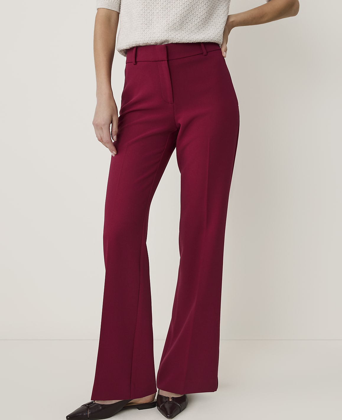 A person in maroon flared trousers and a cream sweater stands against a plain, light background.