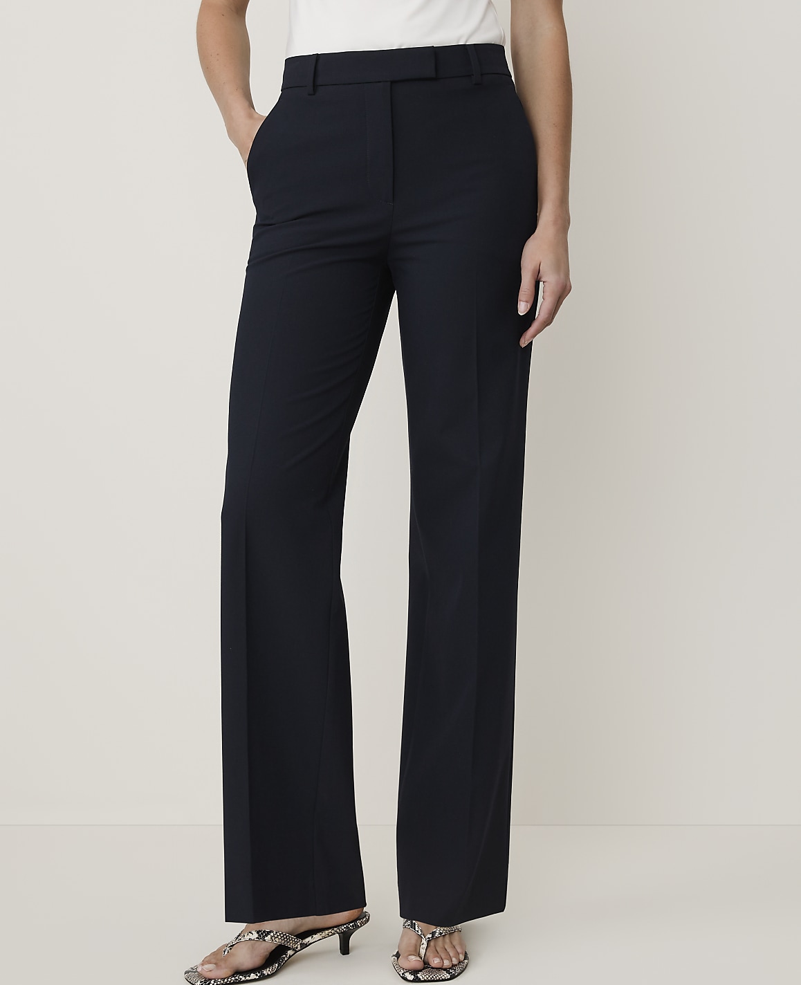 A person stands in dark blue flared trousers and patterned heels against a plain, light background.