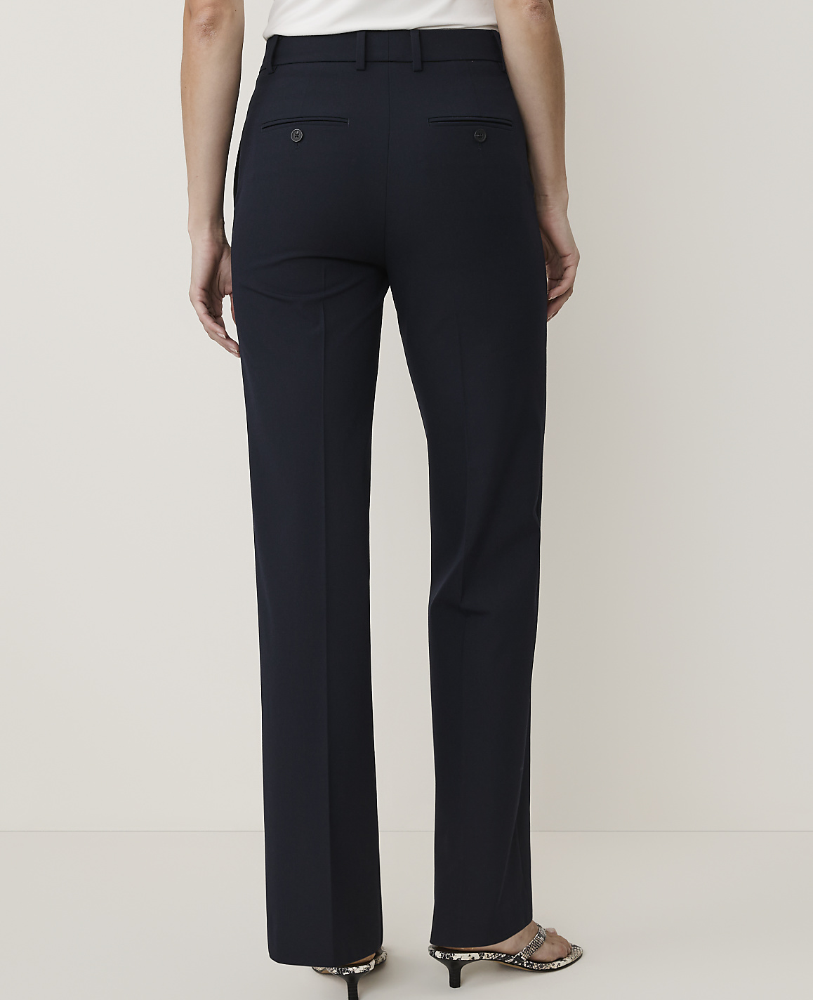 A person wearing dark navy trousers stands against a plain, light-colored background.