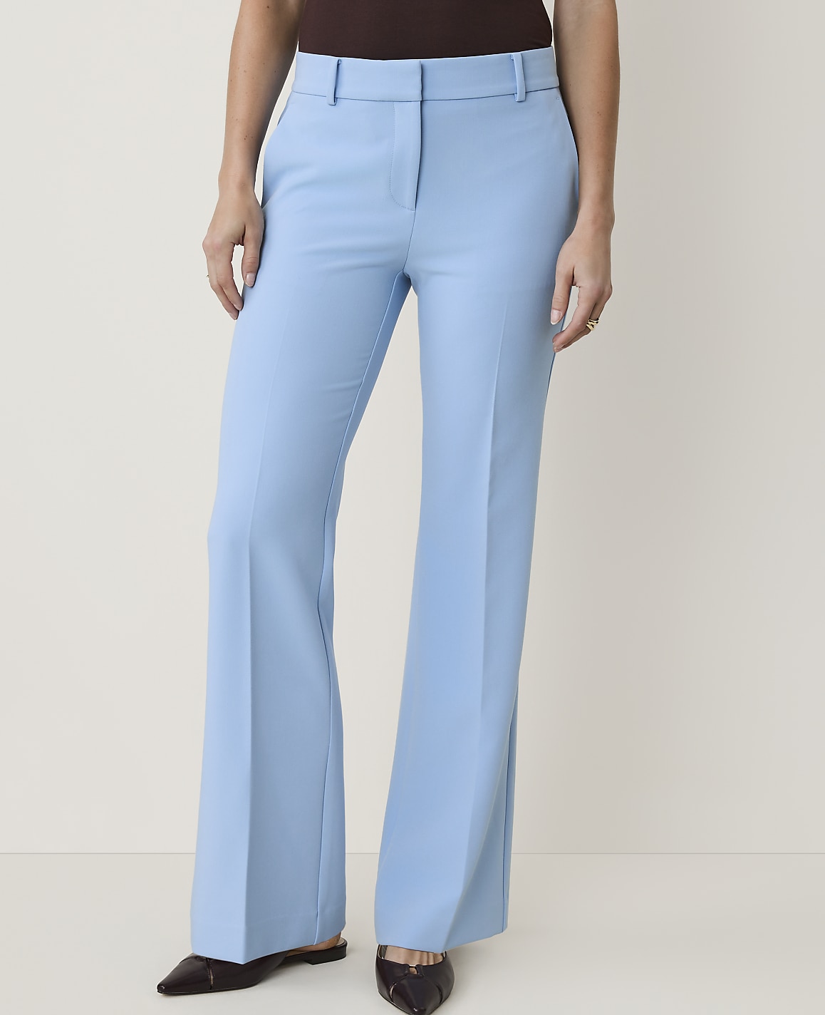 A person stands in light blue flared trousers and dark shoes against a plain white background.