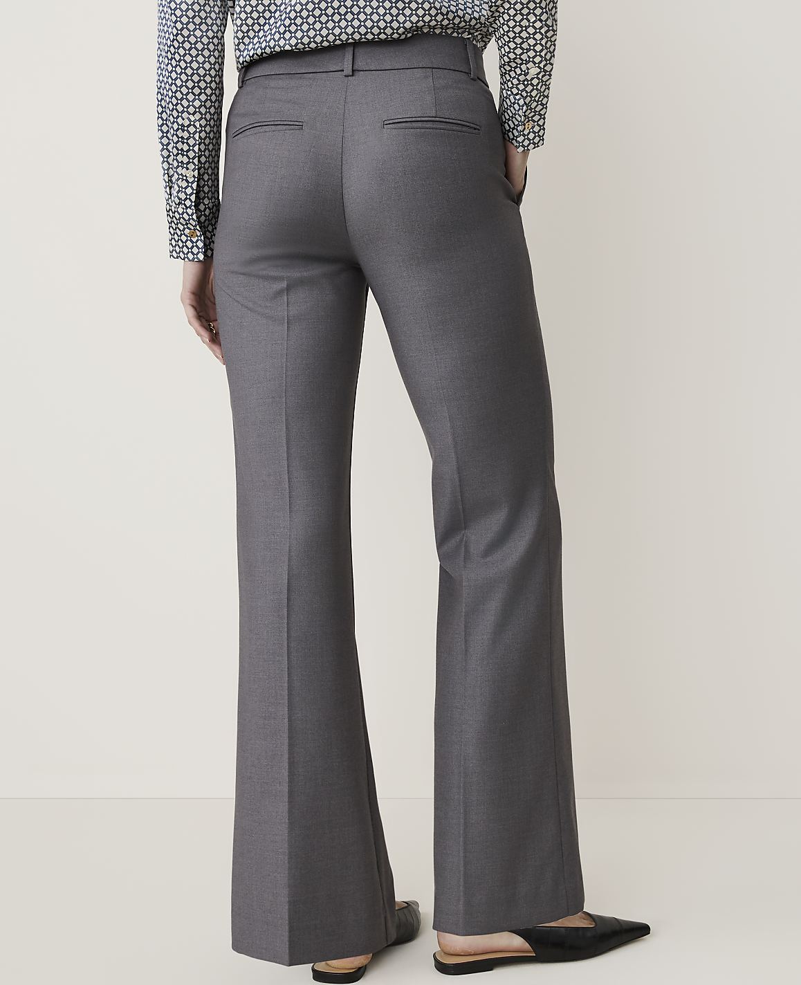 A person wearing gray flared trousers and a patterned shirt stands against a plain, light-colored background.