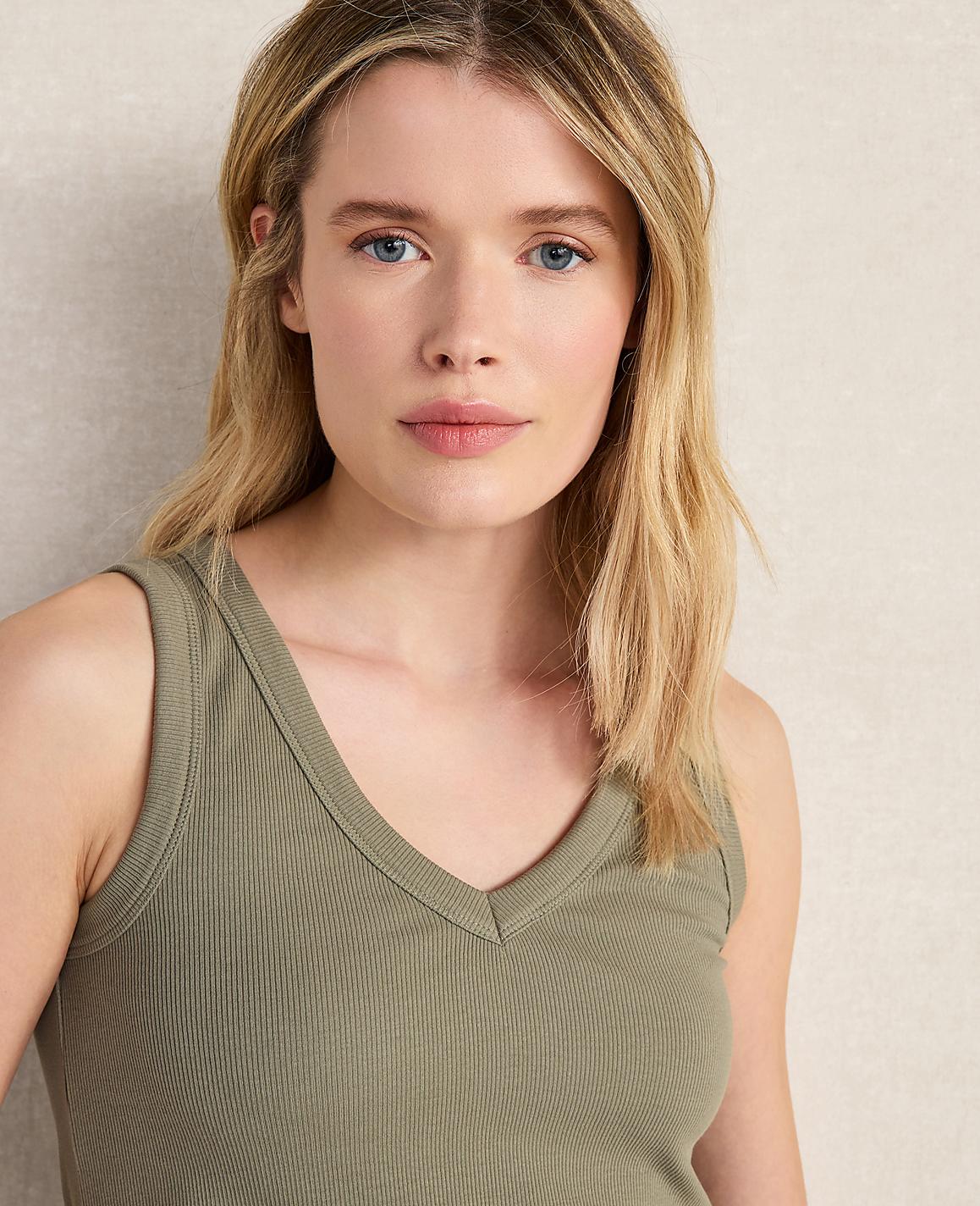 A young woman with blonde hair and blue eyes wears a green tank top in the foreground, with a textured, neutral background behind her.