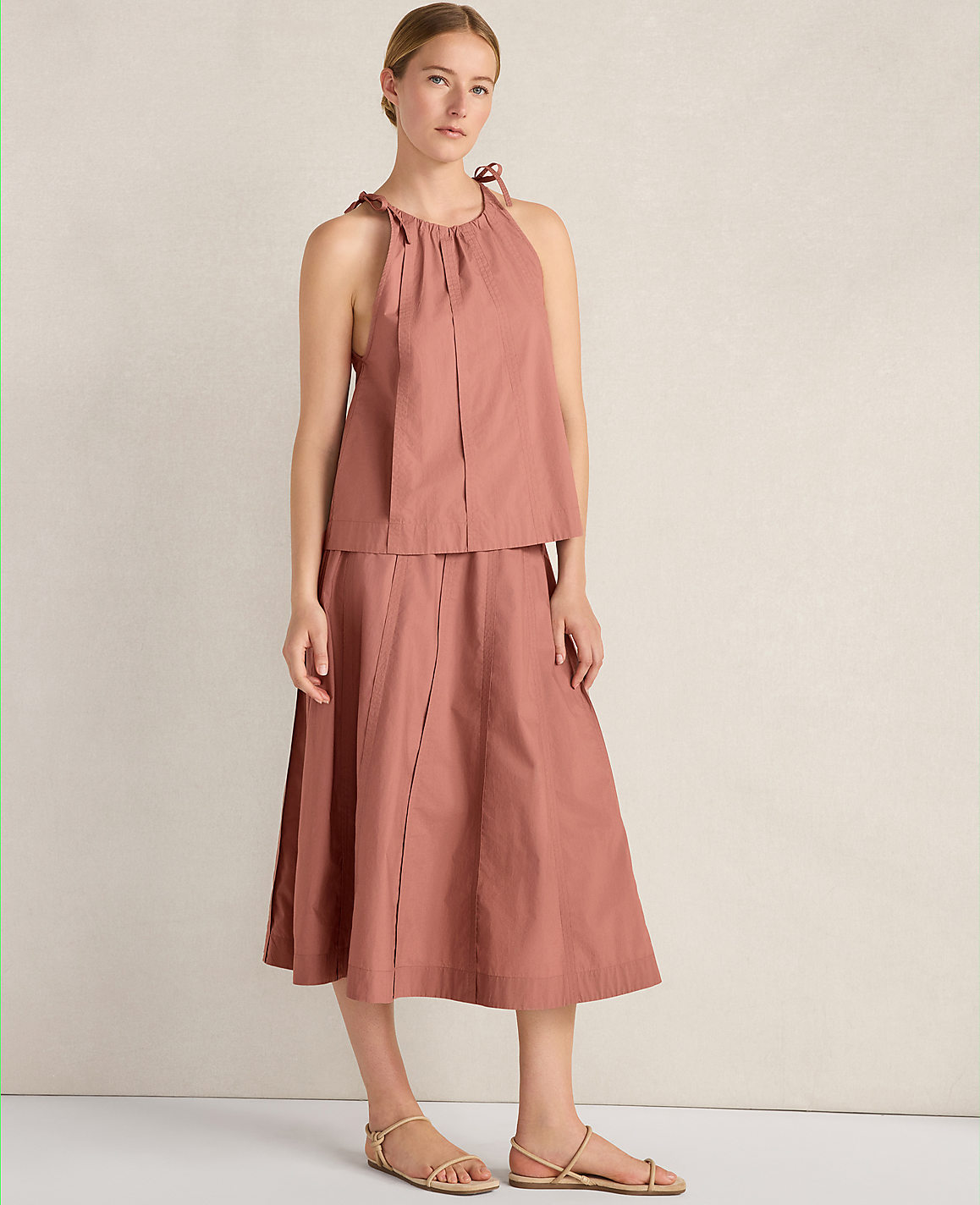 A woman in a rose-colored halter top and skirt stands against a plain, light-colored background.