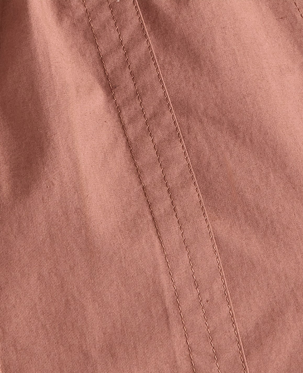 A close-up view of a dusty rose fabric with visible stitching runs diagonally across the frame.