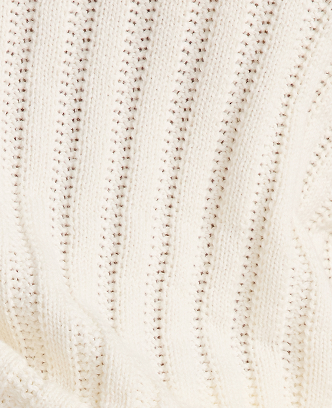 A close-up of a cream-colored knitted fabric with vertical ribbed texture and small, evenly spaced holes fills the frame.