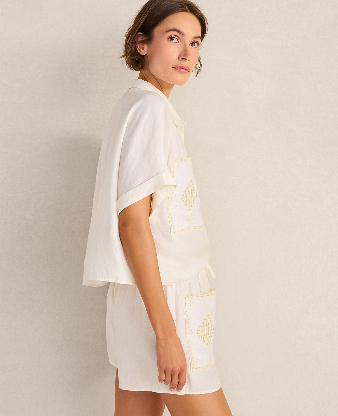 A woman in white pajamas stands against a textured, light-colored wall.