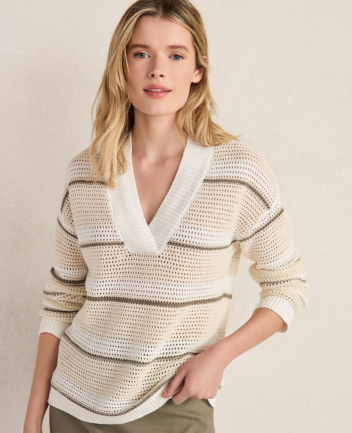 A blonde woman in a striped v-neck sweater stands against a plain, light-colored background.