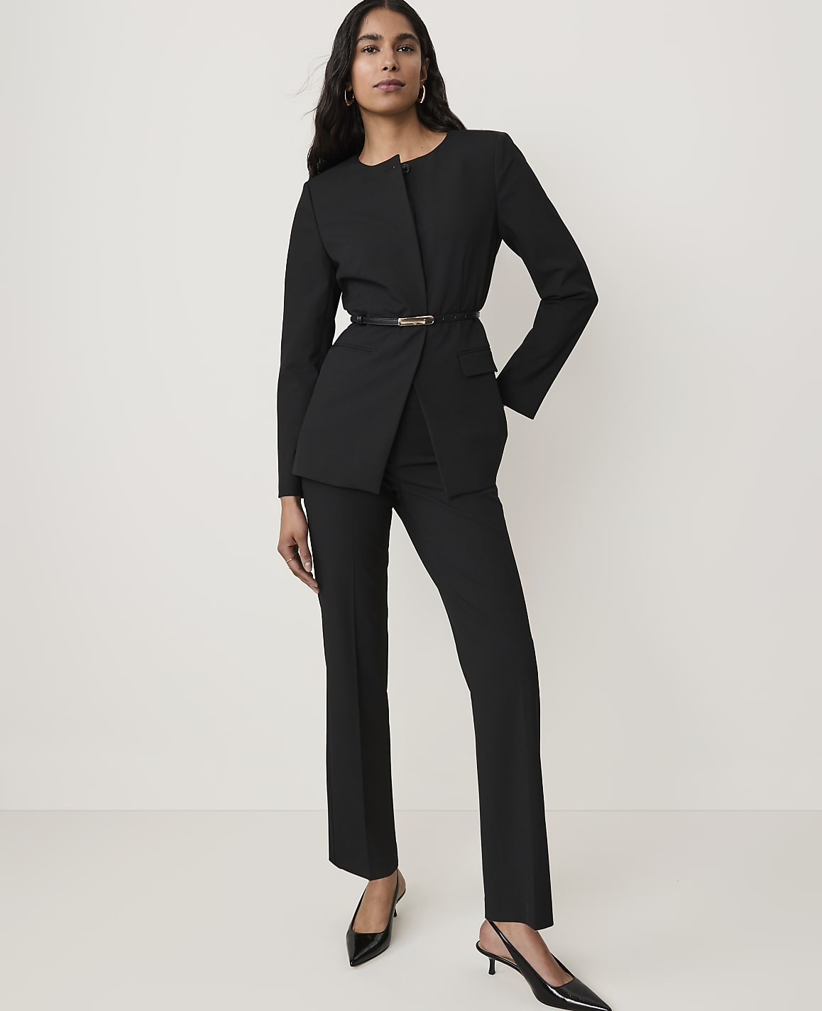 A woman in a black suit stands against a plain white background.