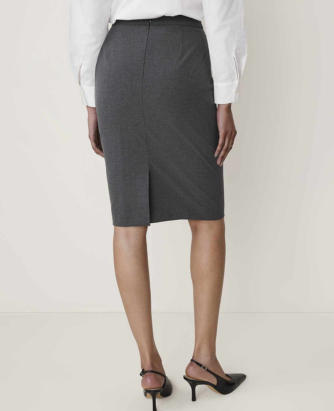 A person wearing a grey pencil skirt and black heels stands against a plain white background.