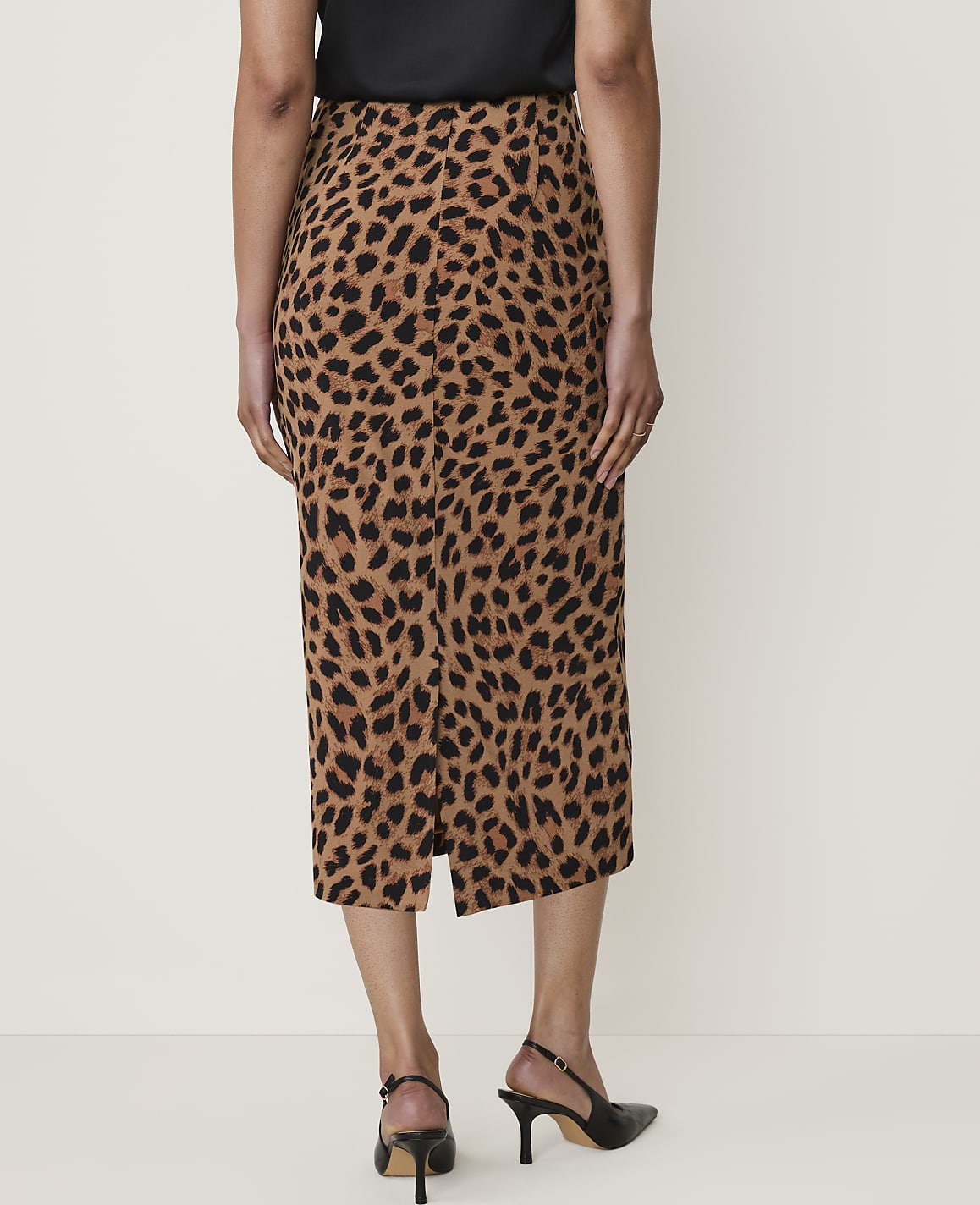 A woman in a leopard print skirt and black heels stands against a plain, light-colored background.