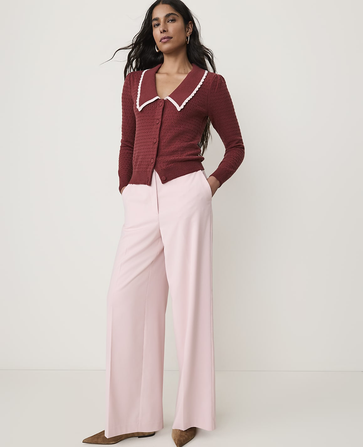A woman in a maroon cardigan and pink wide-leg pants stands against a plain white background.