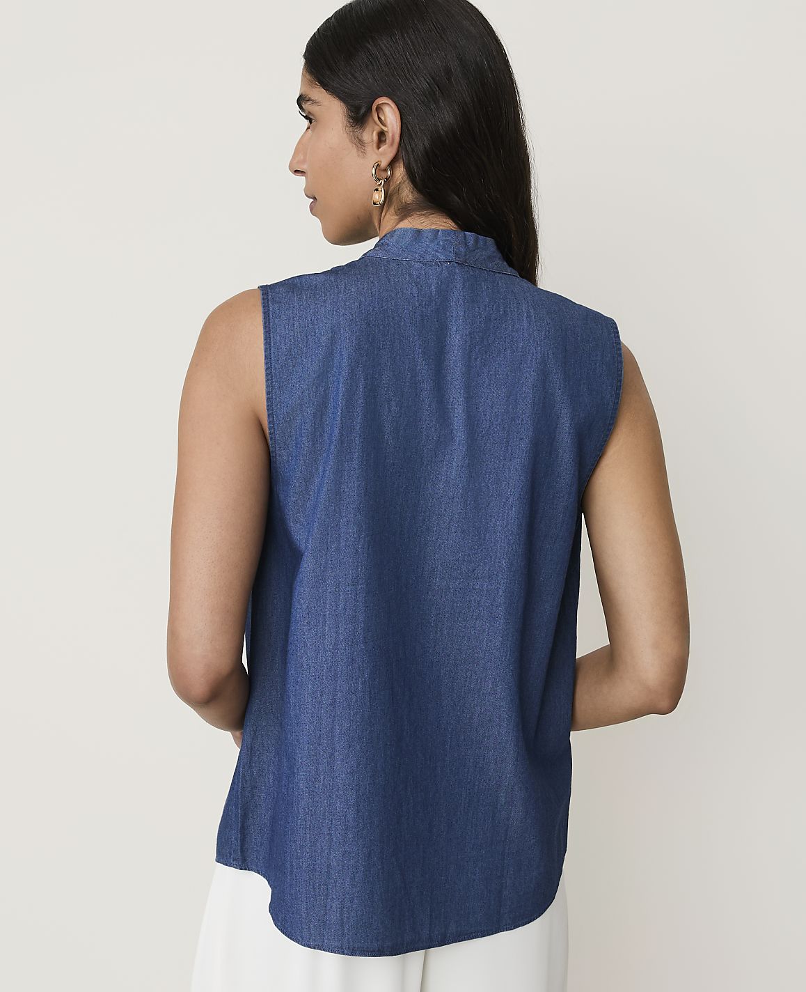 A woman in a denim top stands against a plain, light background.