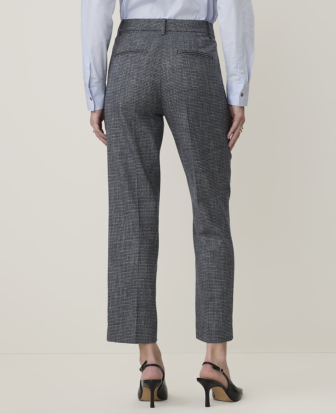 A person wearing patterned gray pants and black heels stands against a plain, light-colored background.