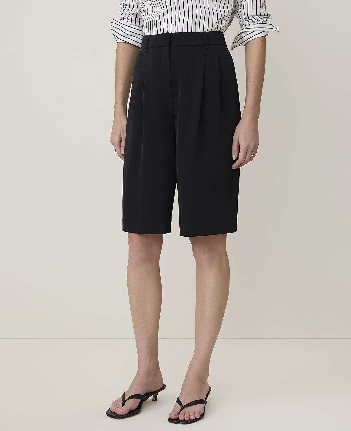 A person stands in black culottes and a striped shirt against a plain, light-colored background.