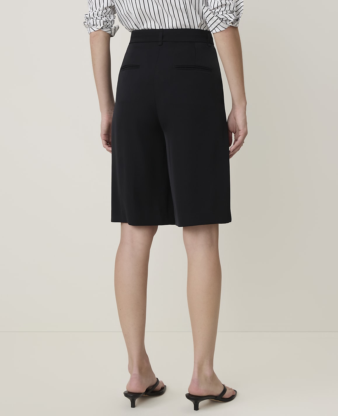 A person wearing black culottes and a striped shirt stands against a plain, light-colored background.