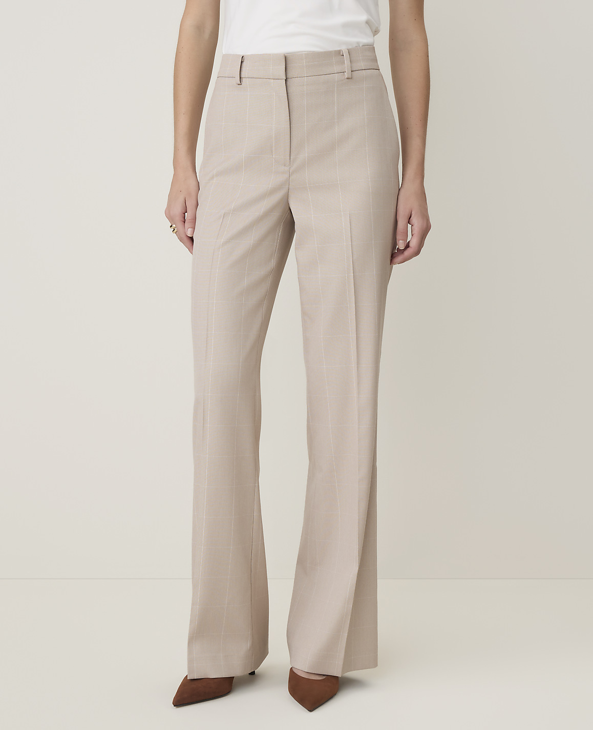A person in beige pinstripe flared trousers and brown pointed-toe heels stands against a plain, light-colored background.