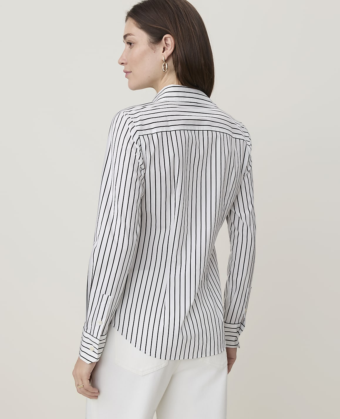 A woman in a striped shirt and white pants stands against a plain, light background.