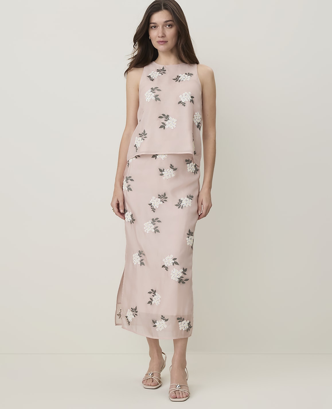 A woman in a floral-patterned pink two-piece outfit stands against a plain, light-colored background.