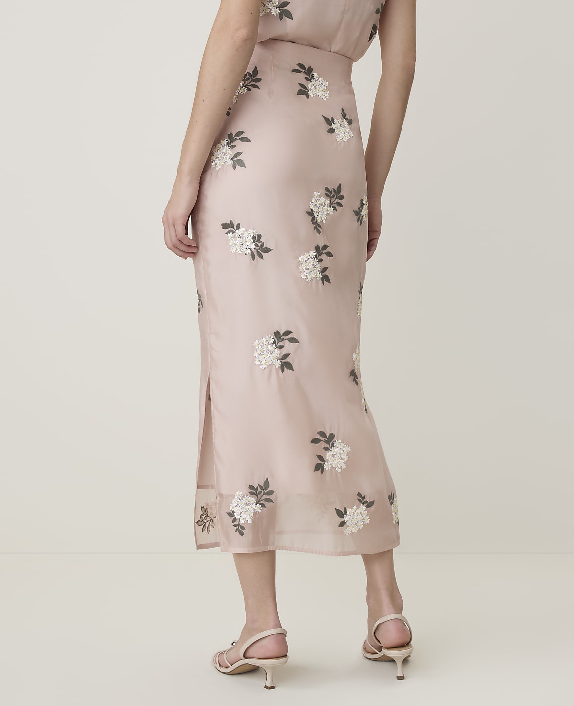 A person in a floral-patterned pink skirt stands against a plain, light-colored background.