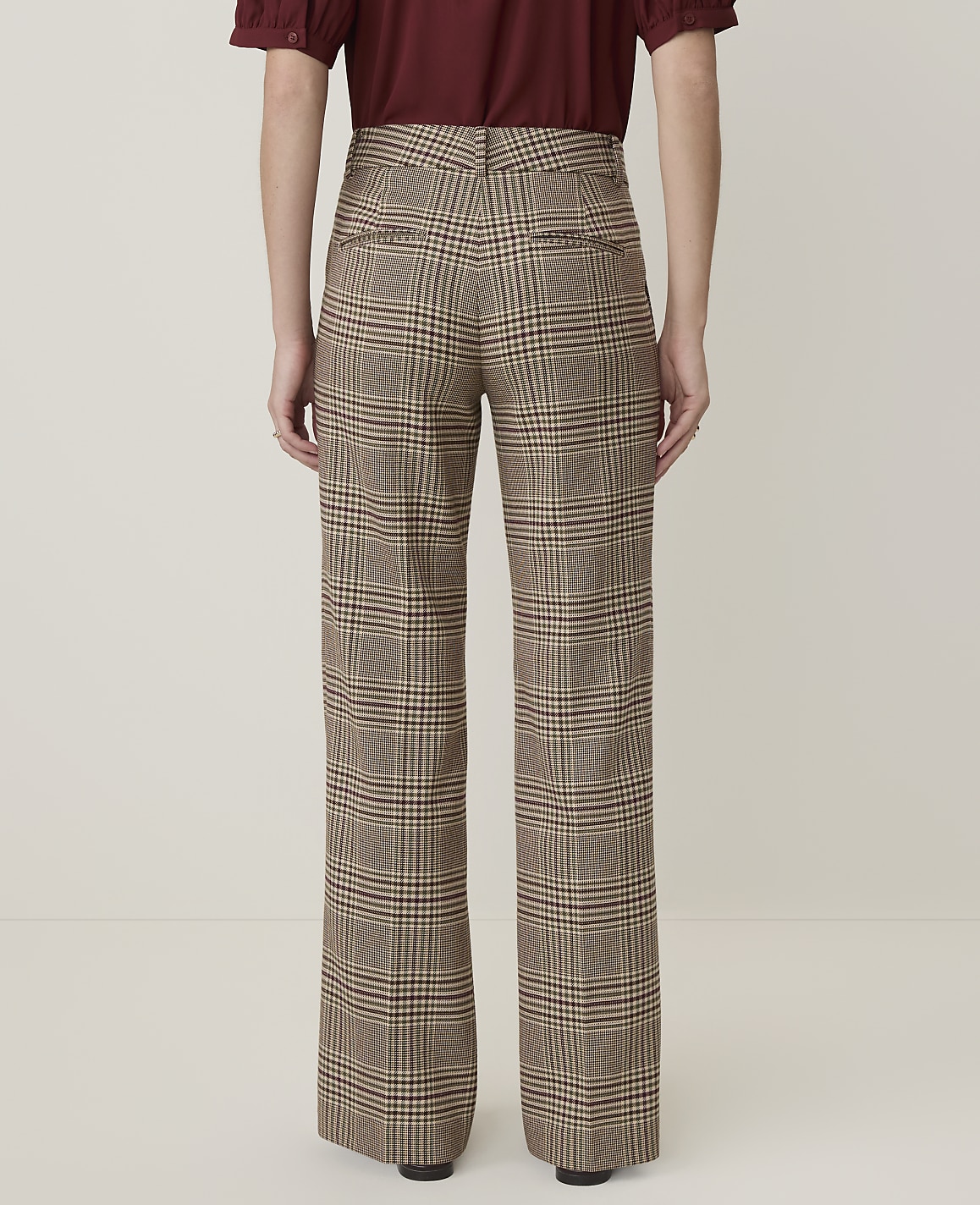 A person wearing plaid wide-leg pants stands against a plain, light-colored background.
