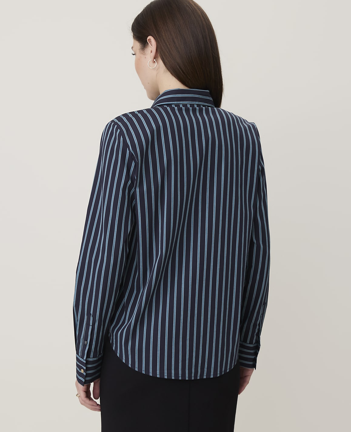 A woman in a dark blue and light blue striped button-down shirt stands against a plain, light gray background.