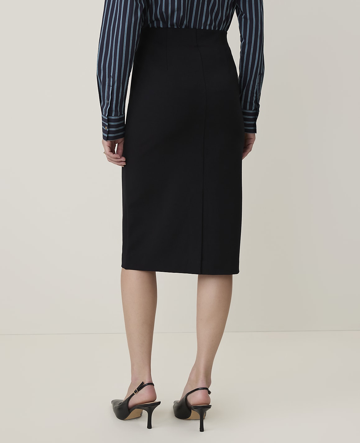 A person wearing a black pencil skirt and a striped blouse stands against a plain, light-colored background.