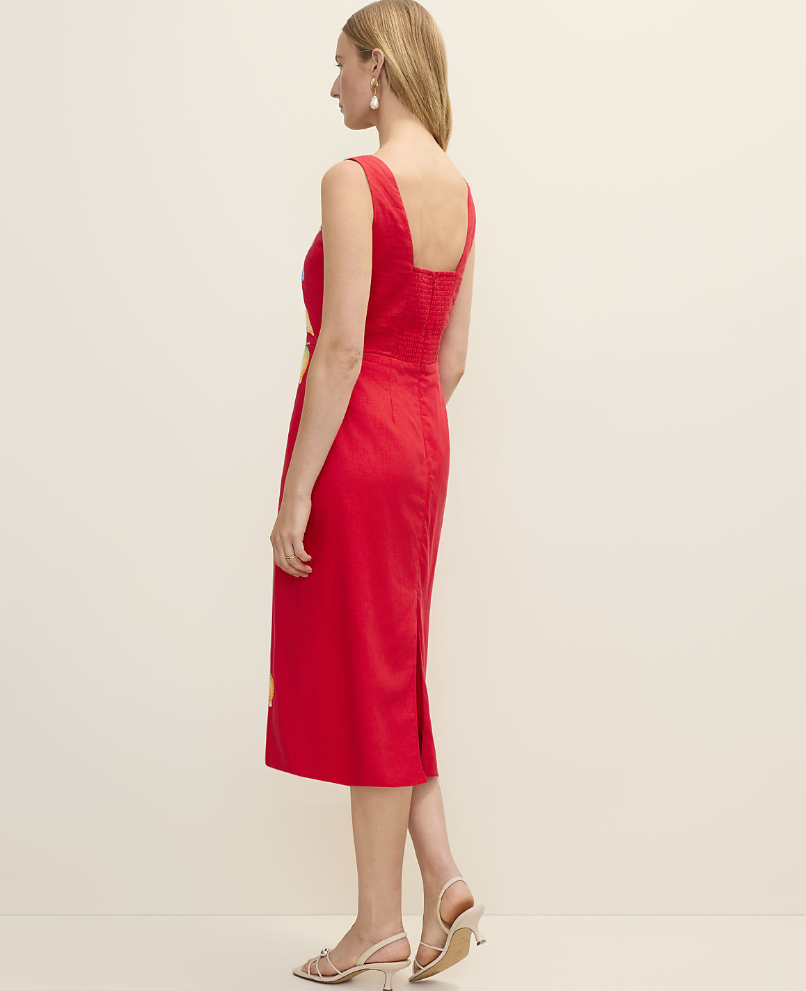 A woman in a red dress stands against a plain, light-colored background.