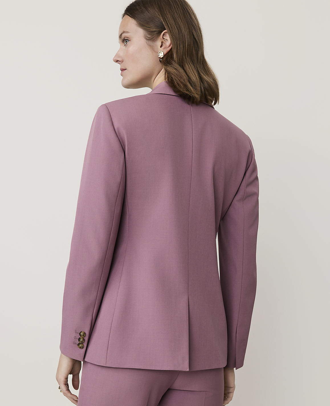 A woman in a mauve blazer and pants stands against a plain, light background.