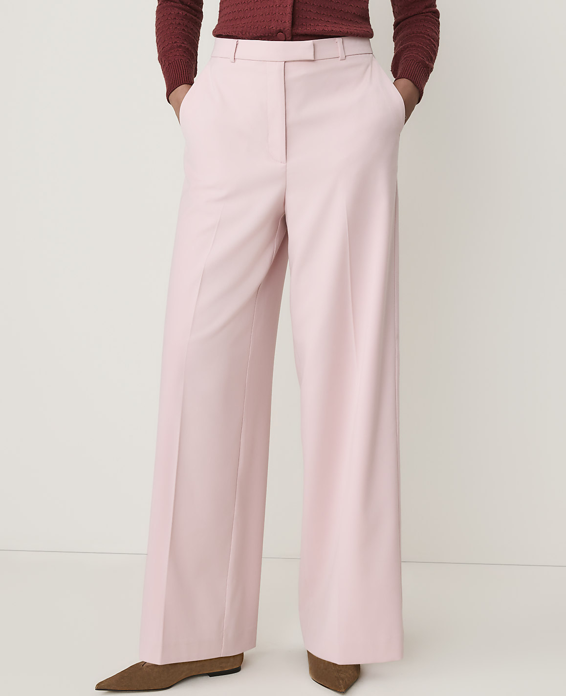 A person stands in light pink wide-leg trousers and a maroon sweater against a plain white background.