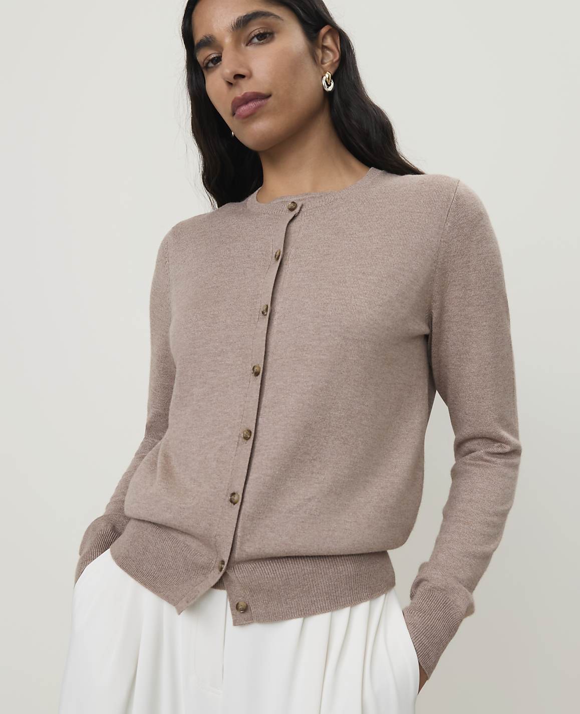 A woman in a beige cardigan stands against a plain, light background.