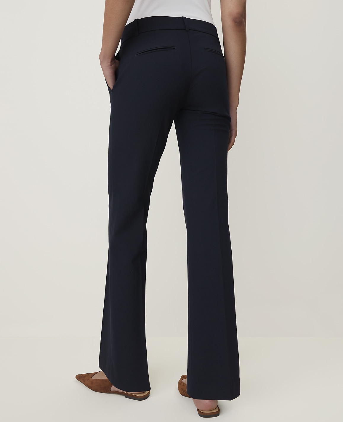 A person wearing dark flared trousers and brown loafers stands against a plain, light-colored background.
