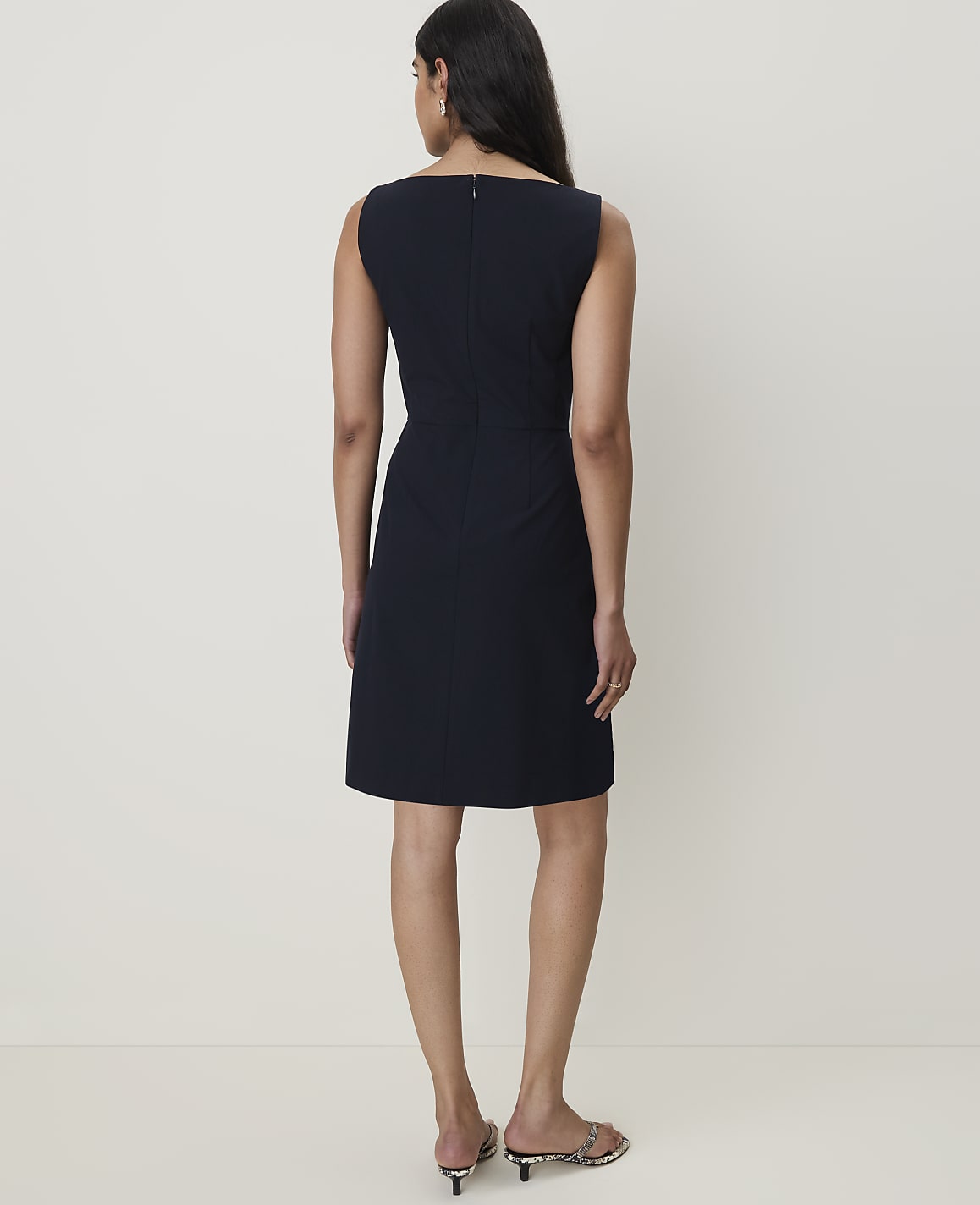 A woman in a dark blue dress stands against a plain, light-colored background.