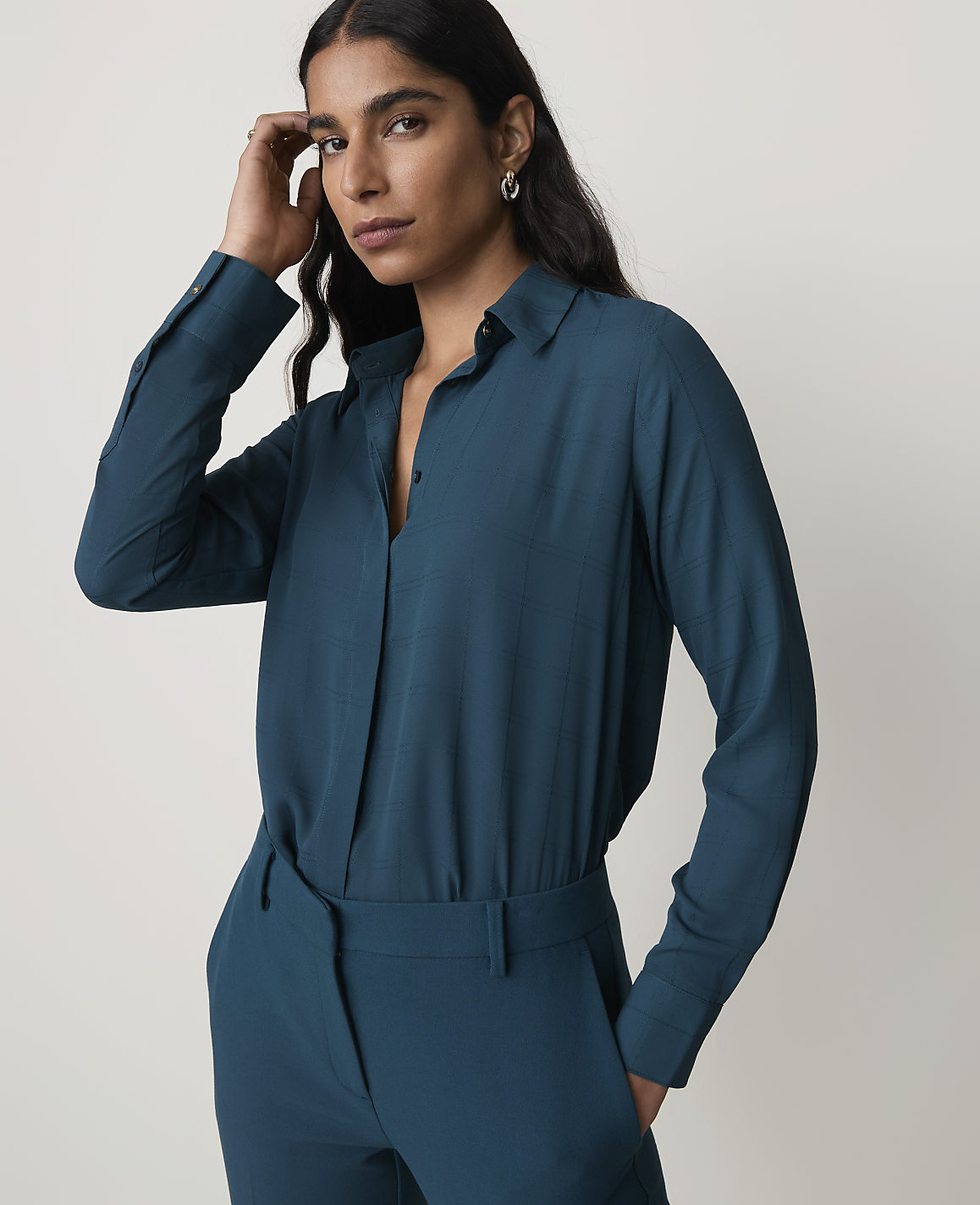 A woman in a teal blouse and matching pants stands against a plain gray background.