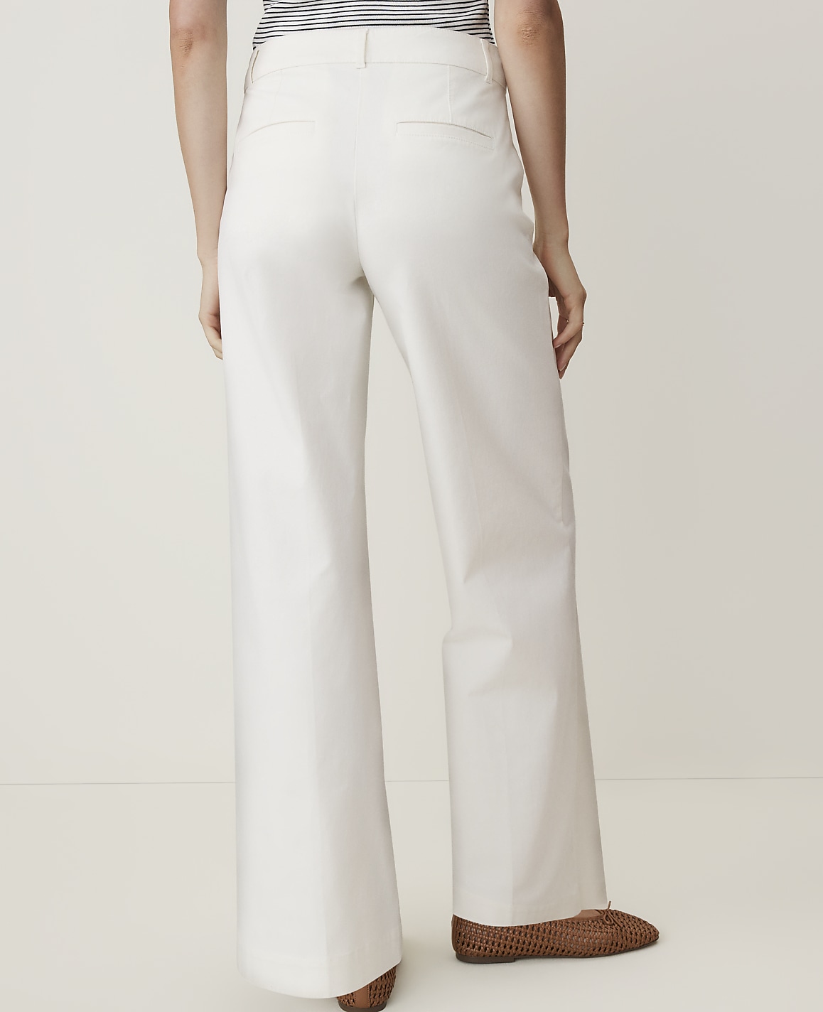 A person wearing white wide-leg pants and brown shoes stands against a plain white background.