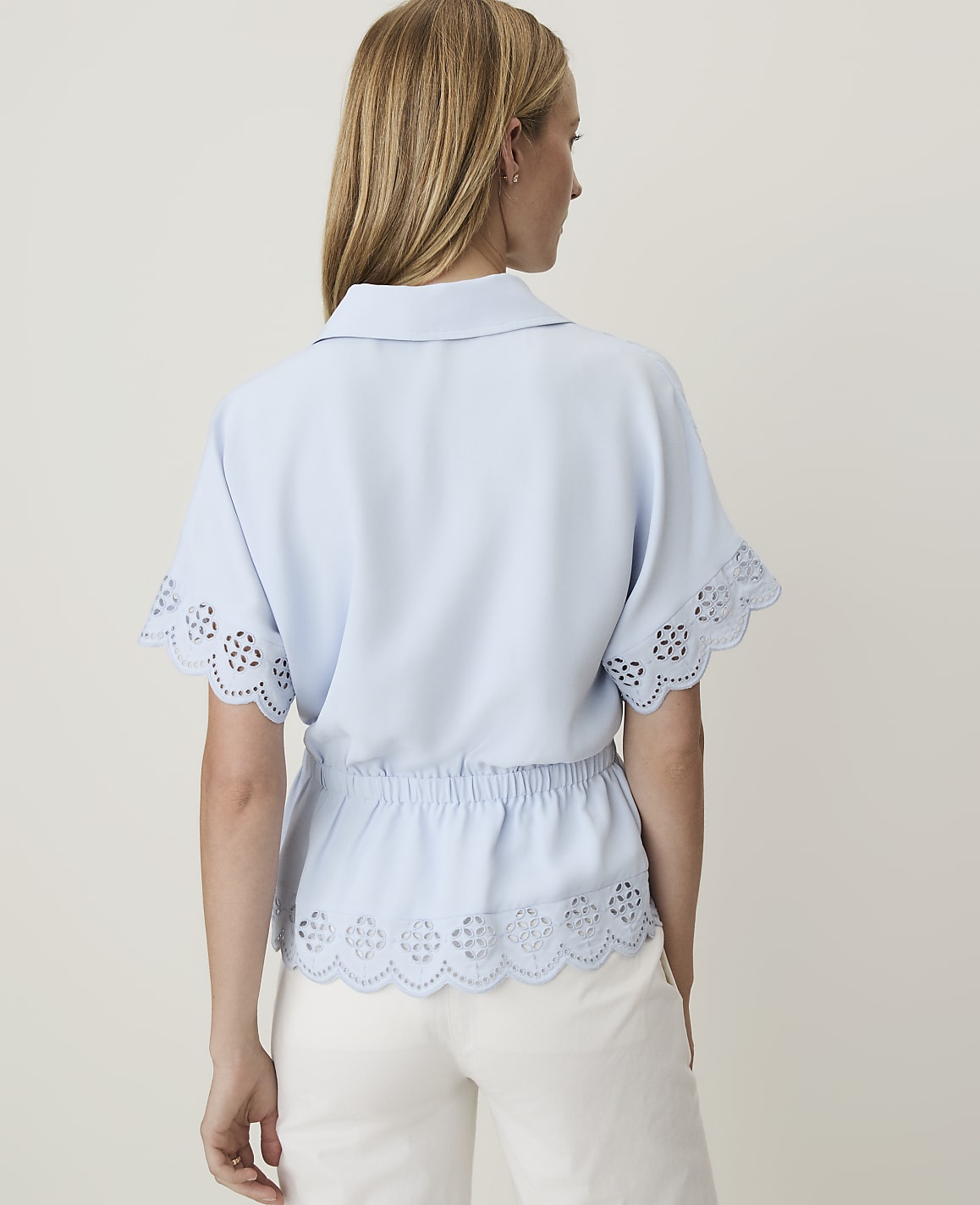 A woman in a light blue blouse with eyelet details stands against a plain, light background.
