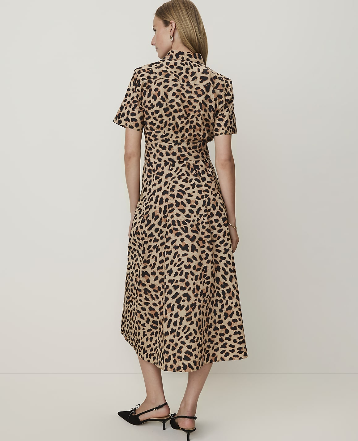 A woman in a leopard print dress stands against a plain, light-colored background.