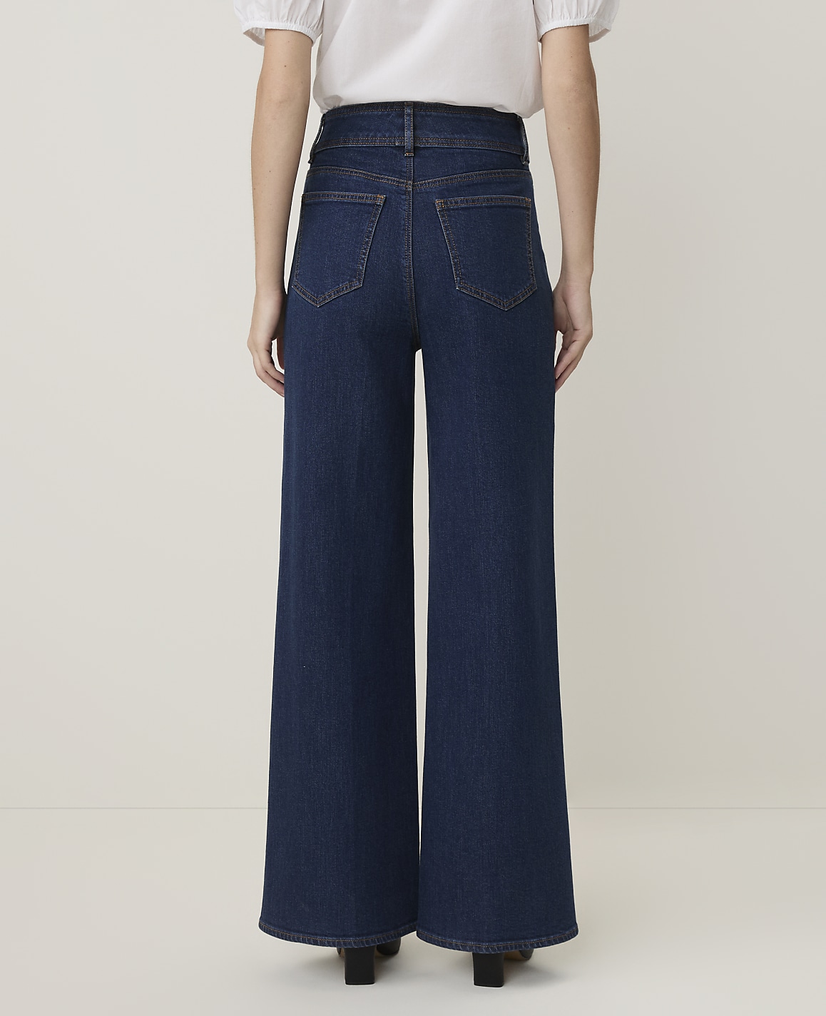 A person wearing dark wash wide-leg jeans stands against a plain, light-colored background.