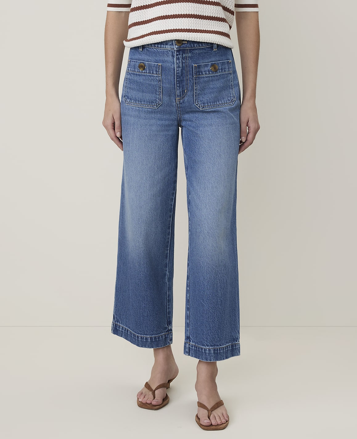 A person wearing wide-leg denim jeans and brown sandals stands against a plain white background.