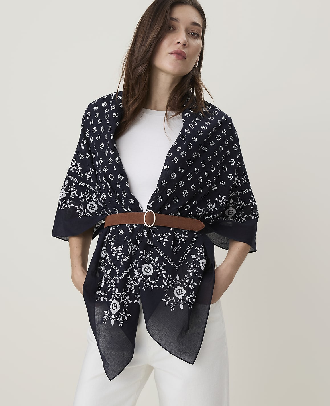 A woman in a white top and white pants wears a dark blue patterned scarf cinched with a brown belt, against a plain white background.