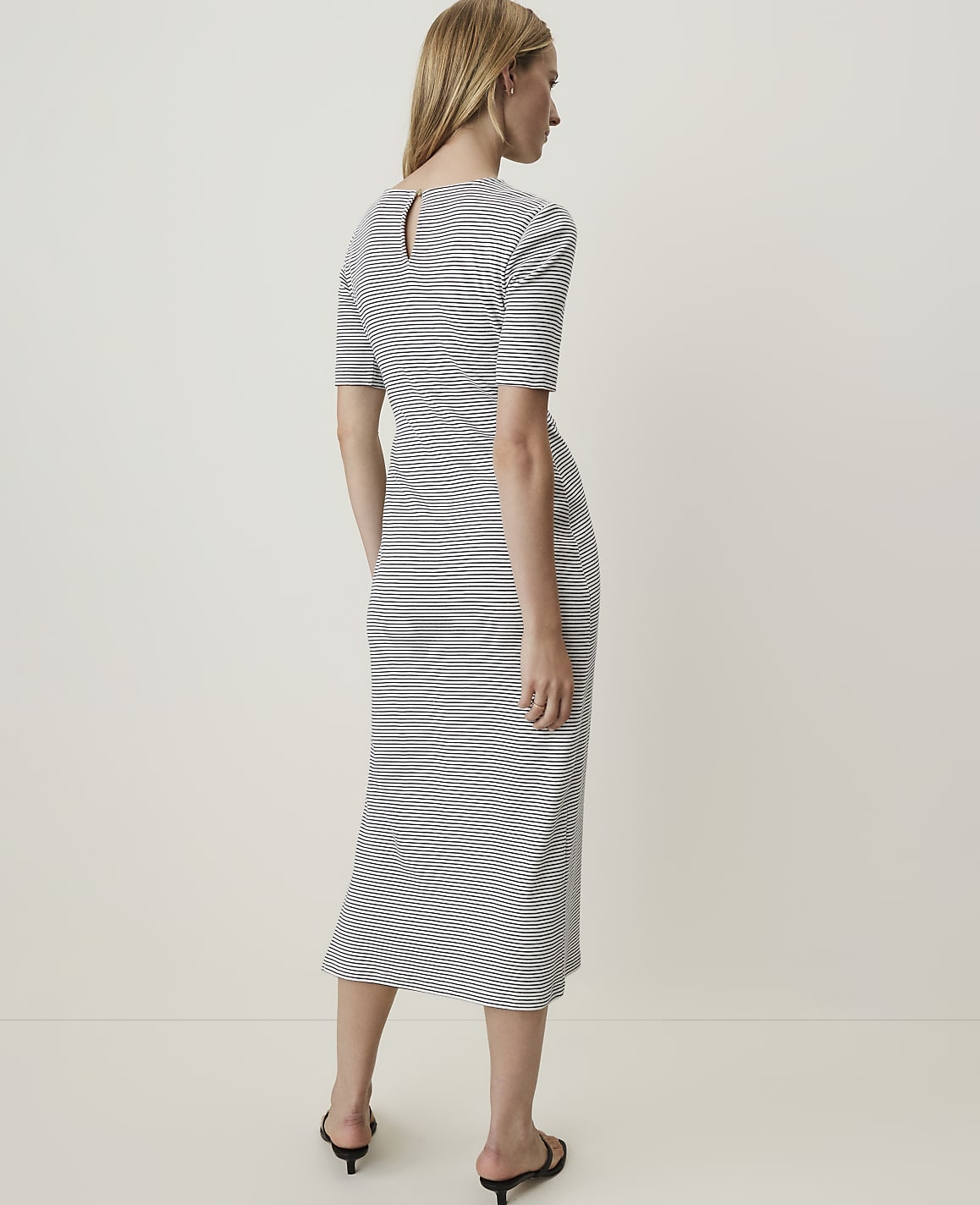 A woman in a striped dress stands against a plain, light-colored background.