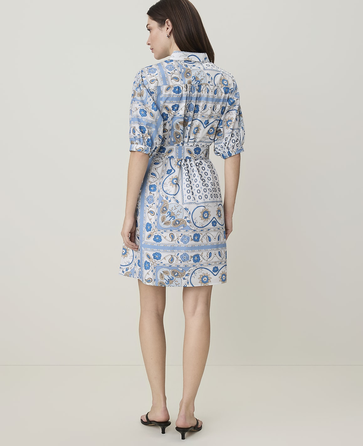 A woman in a blue and white patterned shirtdress stands against a plain, light-colored background.