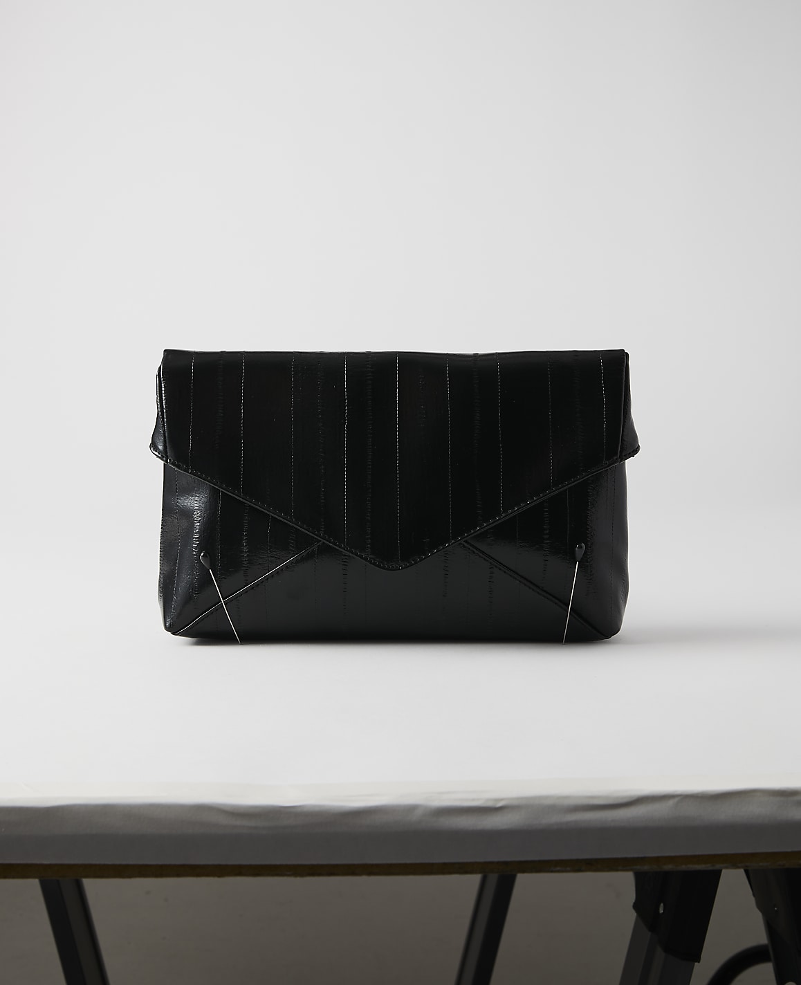 A black, textured envelope clutch rests on a white surface against a plain white background.