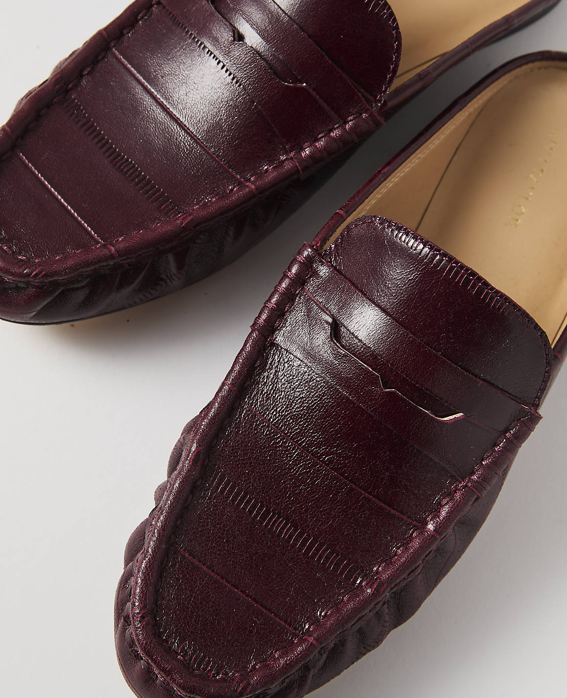 A pair of burgundy leather loafers with a penny strap detail are laid out on a white background.