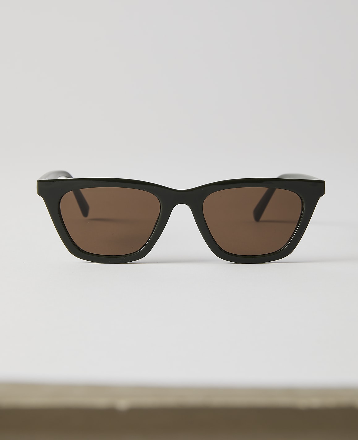 Black-rimmed sunglasses with brown lenses rest on a white surface against a plain white background.