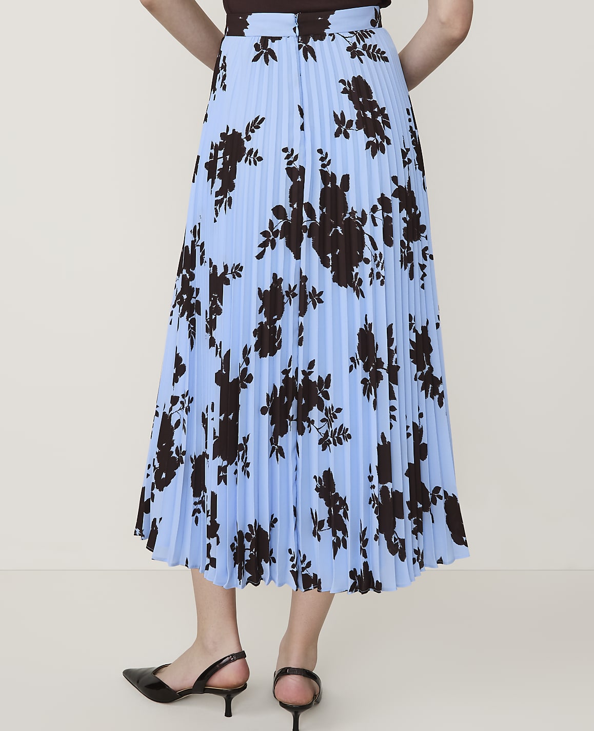 A light blue pleated skirt with a dark floral print is worn by a person standing against a plain white background.