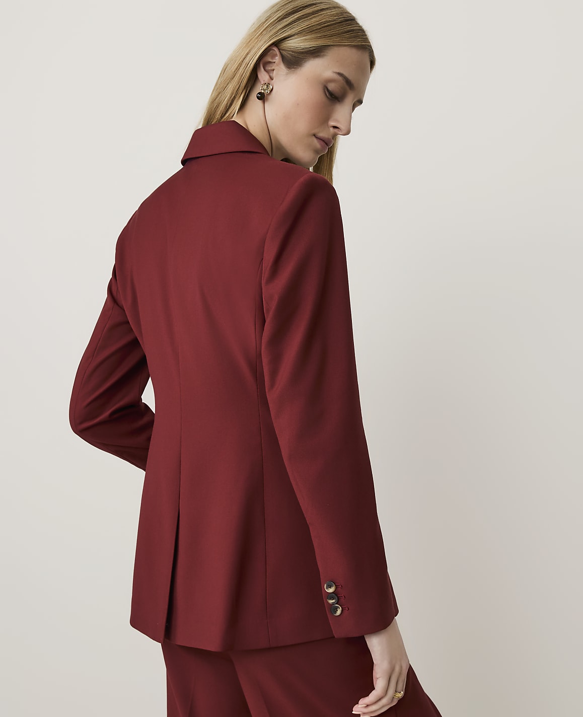 A woman in a maroon blazer and pants stands against a plain, light background.